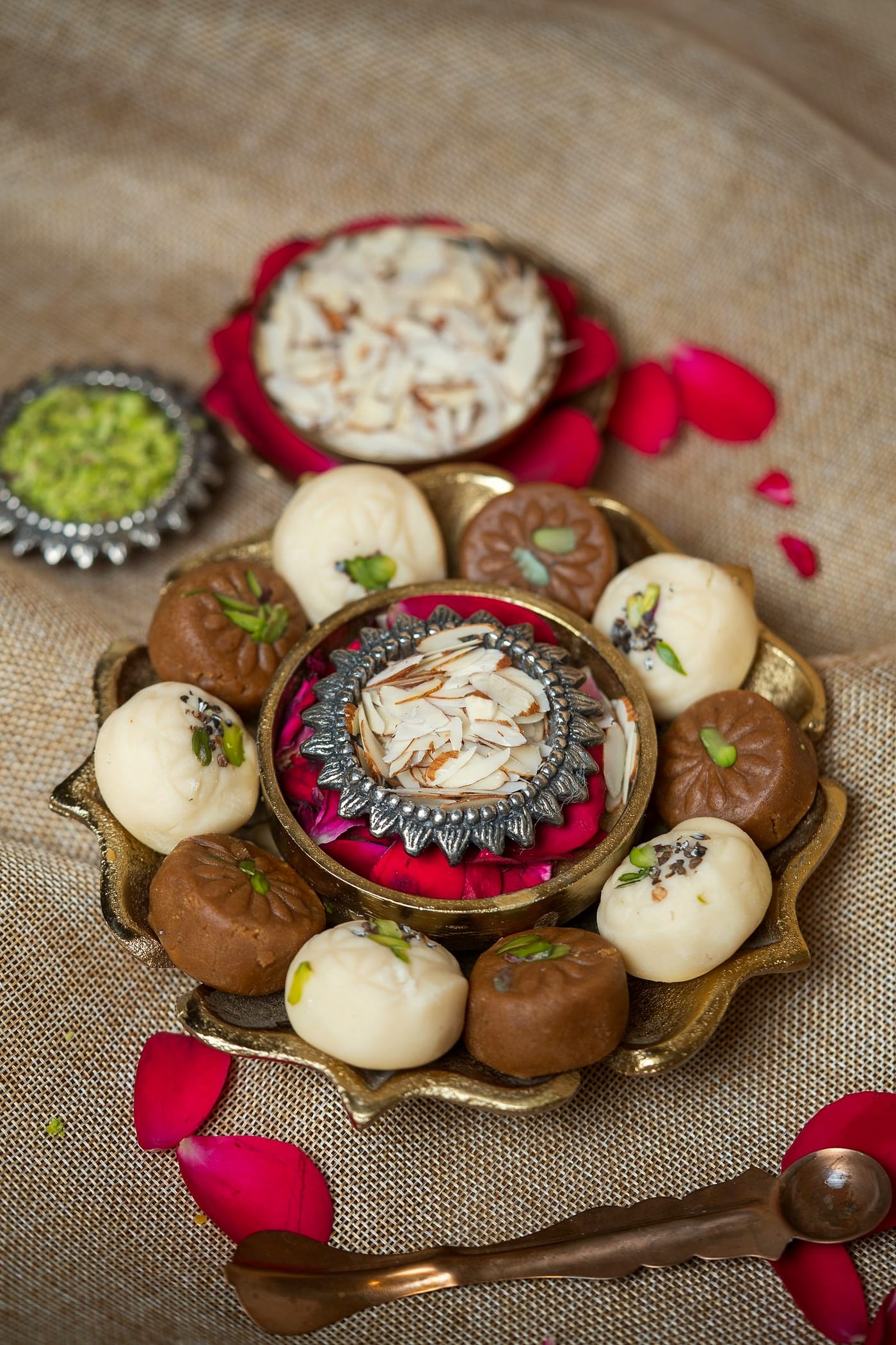 White and nolen gur sandesh arranged around a bowl of almonds on a brass plate.