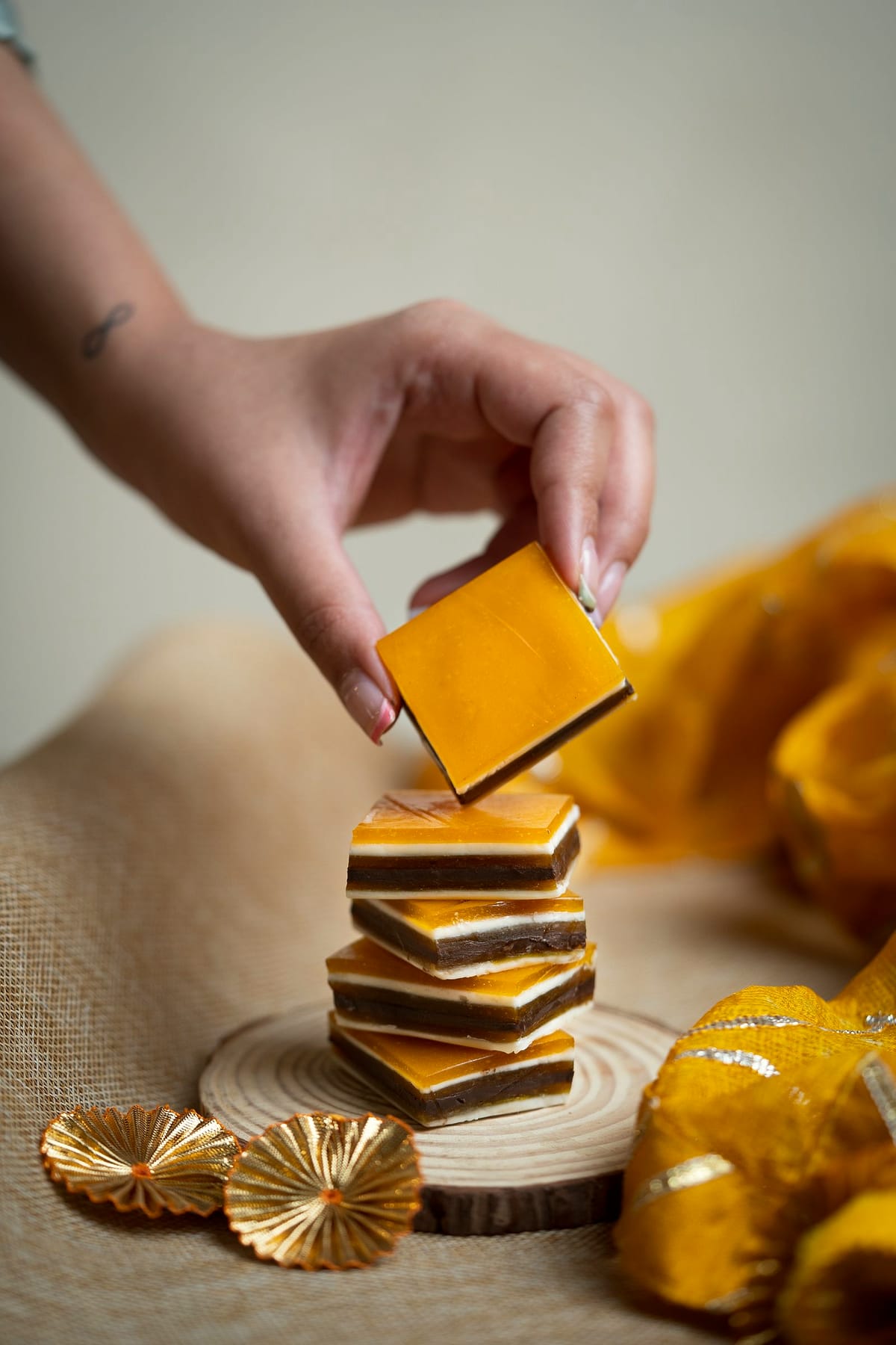 A hand sets the last square on a stack of layered barfi.