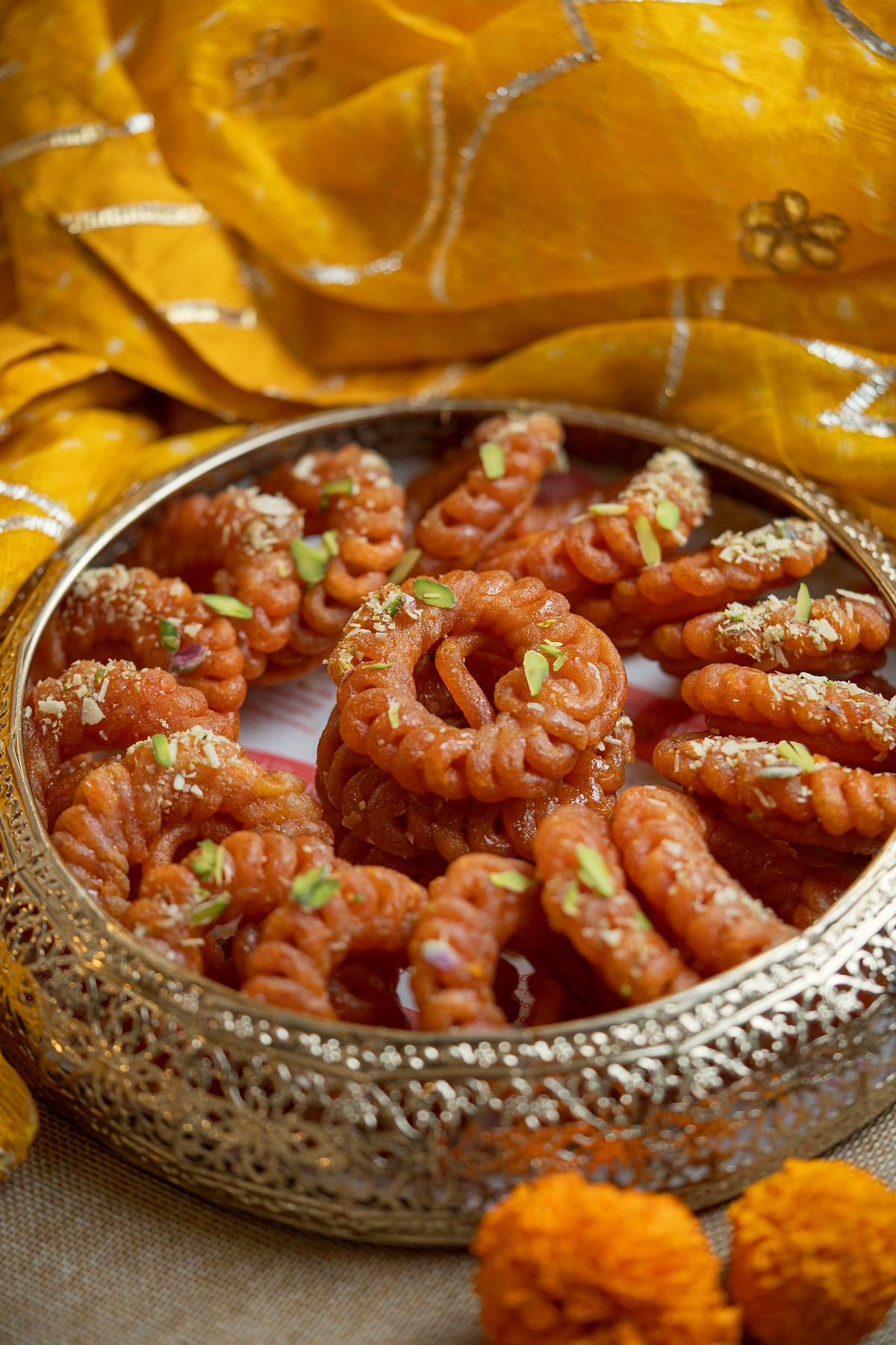 Orange amriti rings piled in a brass bowl on yellow silk.
