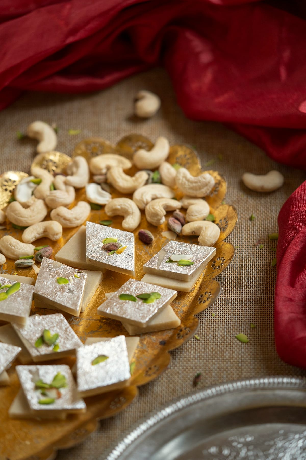 Diamonds of cashew barfi with silver leaf, scattered with cashews.