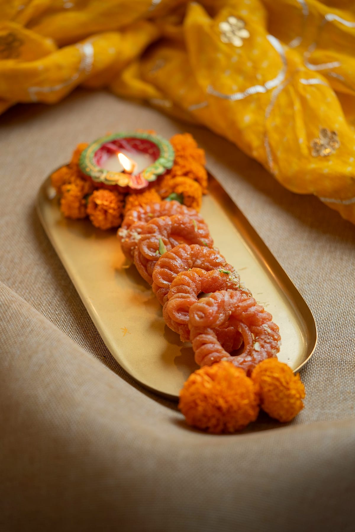 Orange syrup-soaked spirals on a long brass tray with marigolds.