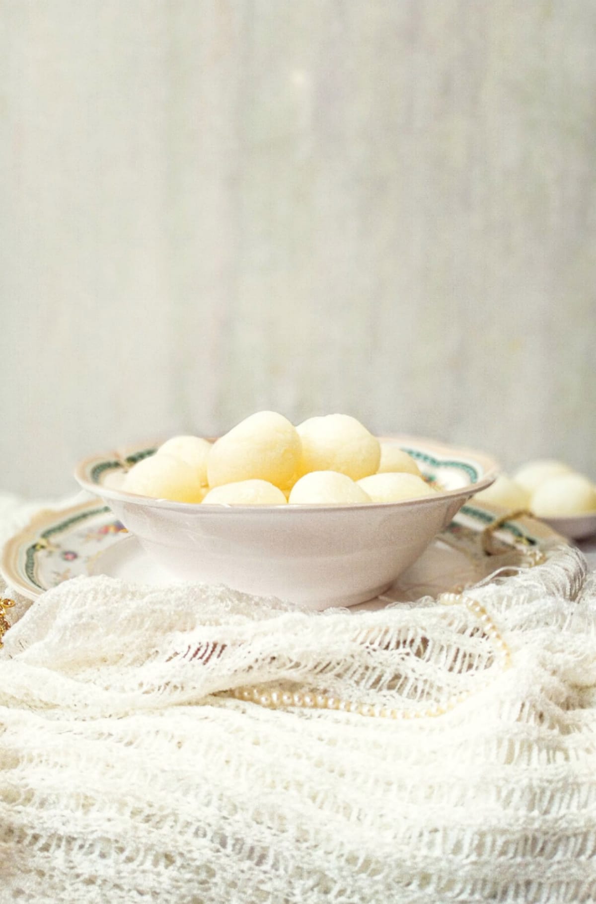 Soft white rosogolla heaped in a china bowl on a white lace cloth.