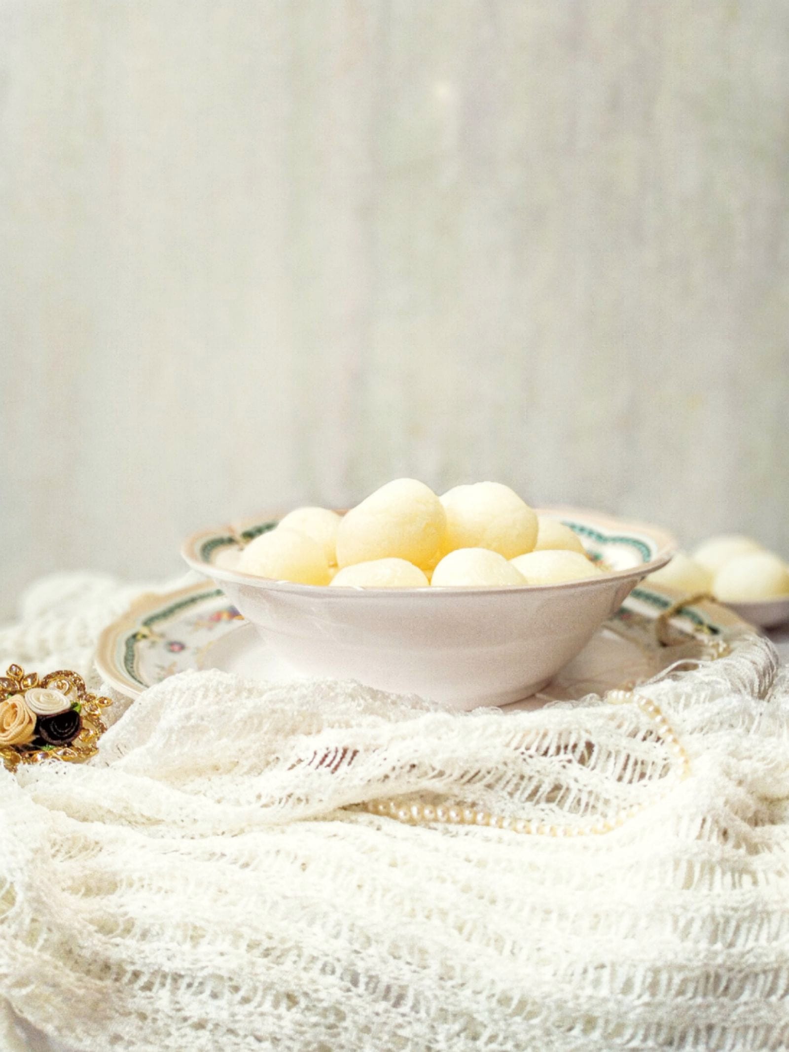 Soft white rosogolla heaped in a china bowl on a white lace cloth.