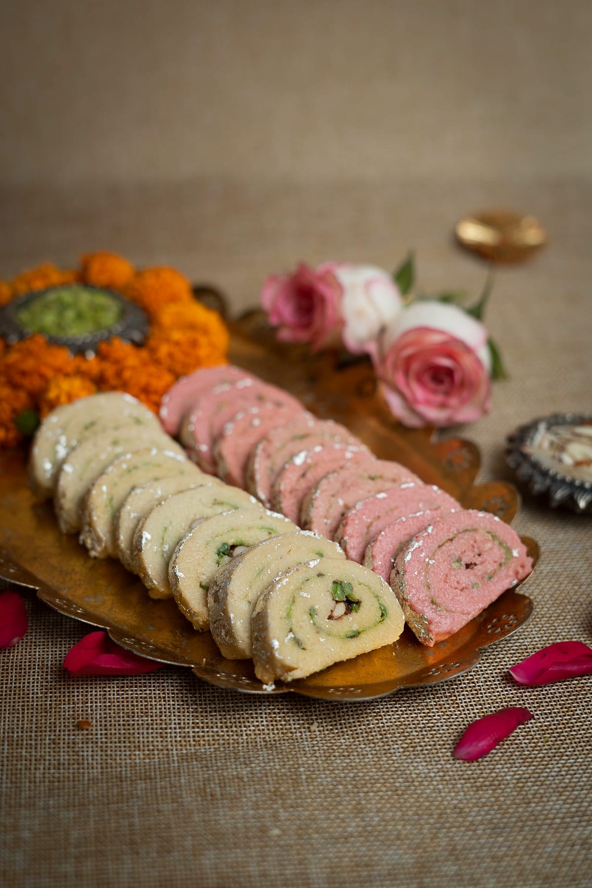 Sliced pistachio and rose sandesh rolls in rows on a brass tray.